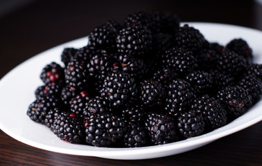 Fresh blackberries in a white bowl on dark background