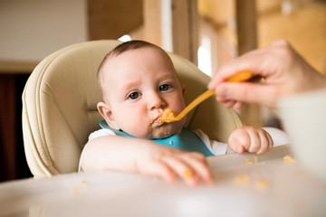 Unrecognizable mother at home feeding her baby son.