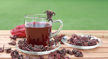 Roselle juice in cup and dry roselle on wooden plank against green grass background.