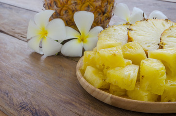 Sliced pineapple on wooden plate decorated with beautiful flowers.