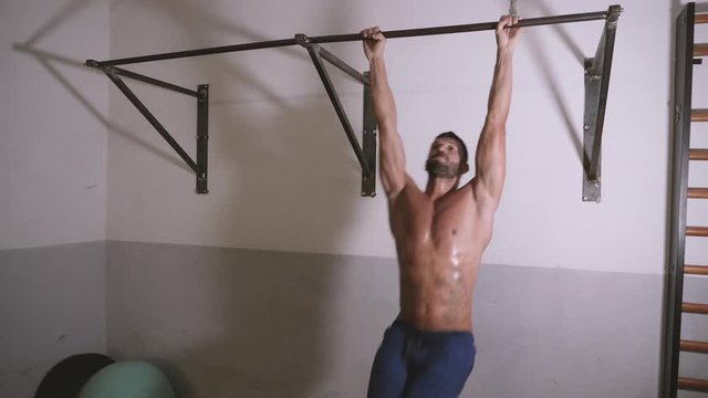 Athletic muscular man with perfect fitness body performing abdominal exercises on the horizontal bar at the gym.