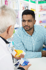 Customer Looking At Senior Pharmacist Holding Medicines
