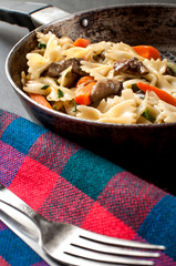 close up photo of a fresh cooked pasta with mushrooms and vegetables in a pan ahead of vintage silver cutlery, vertical image