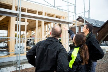 Female Carpenter Pointing At Incomplete Building While Standing 