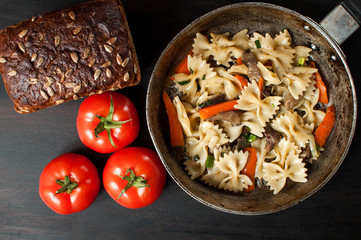 fresh cooked pasta with mushrooms and vegetables in a pan, along with tomatoes and bread with bran, horizontal image