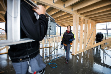 Fototapeta premium Female Carpenter Smiling While Male Colleague Carrying Ladder