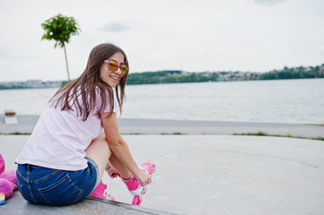 Portrait of a beautiful girl wearing sunglasses, t-shirt and shorts putting on rollerblades outdoor...