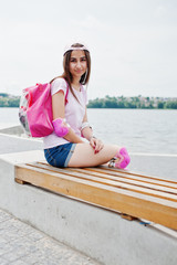 Fantastic young woman in casual clothing and cap sitting on the bench in the skatepark with...