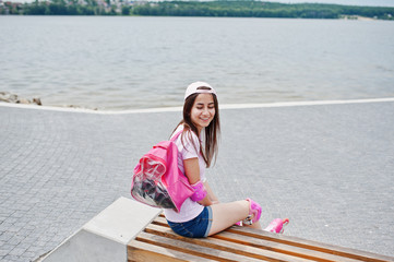 Fantastic young woman in casual clothing and cap sitting on the bench in the skatepark with...