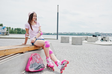 Fantastic young woman in casual clothing and cap sitting on the bench in the skatepark with...