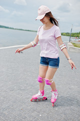 Portrait of a good-looking young woman in casual clothing rollerblading on the pavement in the park.