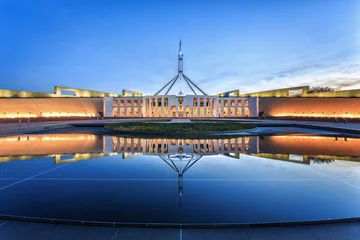 Dramatischer Abendhimmel über dem Parlamentsgebäude, beleuchtet in der Dämmerung. Es war das teuerste Gebäude der Welt, als es 1988 in Canberra, Australien, fertiggestellt wurde © CHATCHAI