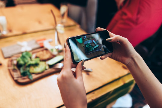 Food photography for social networks. Close-up image of female hands holding phone with food on screen taking picture of healthy meal