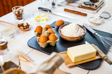 Baking ingredients in rural kitchen - dough recipe ingredients (eggs, flour, milk, butter, sugar) and rolling pin on wooden white table.