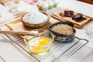 Baking ingredients in rural kitchen - dough recipe ingredients (eggs, flour, milk, butter, sugar) and rolling pin on wooden white table. Close up