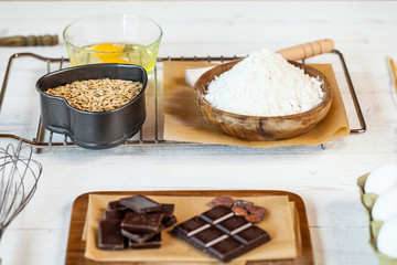Baking ingredients in rural kitchen - dough recipe ingredients (eggs, flour, milk, butter, sugar) and rolling pin on wooden white table.