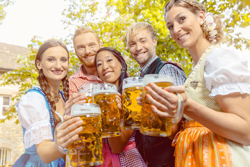 Freunde, zwei Männer, drei Frauen, stehen im Biergarten mit Maßkrügen