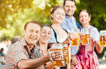 Im Biergarten - Freunde in Lederhosen und Dirndl trinken eine frische Maß Bier