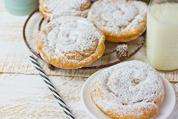 Traditional Spanish or Philippine pastry ensaimada. Powdered, on cooling rack and plate. Glass of milk, top view, white wood background.