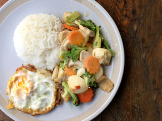mixed fried vegetable tofu with rice and fried egg in white dish on wooden background. Vegetarian Food, healthy food.