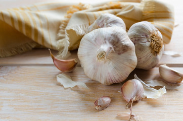Garlic cloves and garlic bulb with linen napkin on wooden background with copy space.
