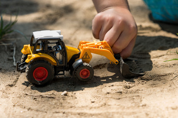 Children play with front loader yellow tractor toy in sand