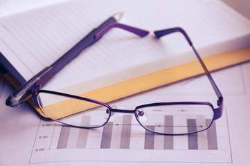 Preparation of business report. A pile of documents, a notebook and glasses on the table.