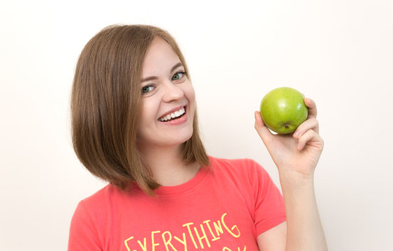 Portrait of smiling pretty girl with bob hairstyle and green apple in her left hand as if suggesting healthy life, fruit diet or tasty apple. White background