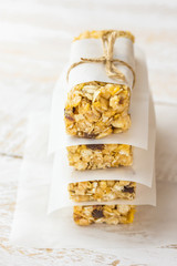 Stacked homemade muesli cereal bar with oats, nuts, raisins, honey and dried apples. Lined with parchment paper, tied with twine. White plank wood background. Healthy vegetarian snack.