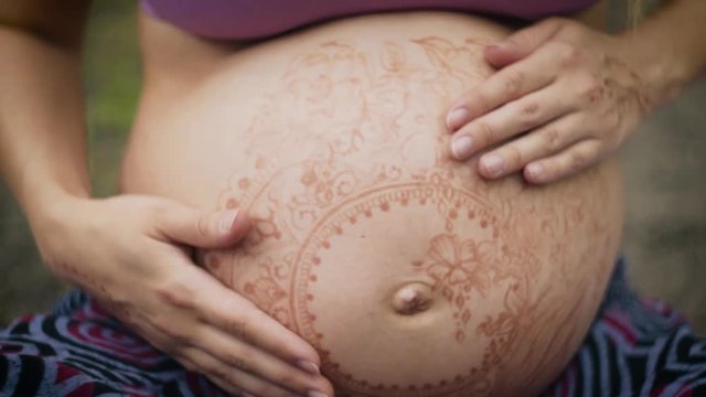 Caucasian pregnant woman with dreadlocks in boho style. White mehendi on big belly. Expectation of baby in new age lifestyle. Conscious parents concept.