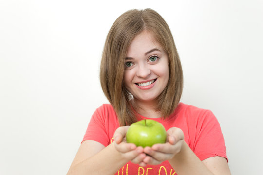 Portrait photo of smiling pretty girl with bob hairstyle holding green apple in both hands as if suggesting it, healthy lifestyle or fruit diet. White background