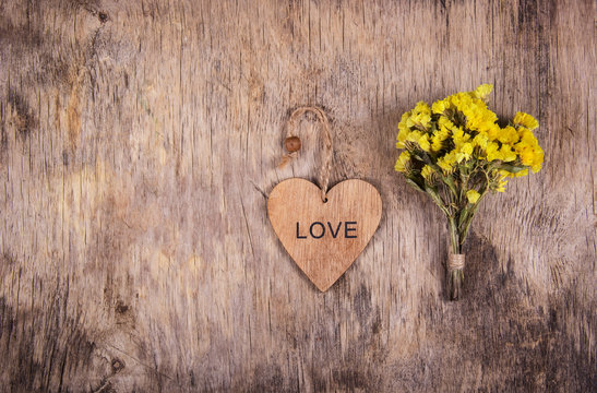 Wooden heart and yellow flowers on an old worn wooden background. Backgrounds and textures. Copy space