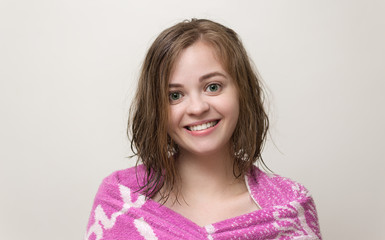 Portrait photo of smiling pretty girl with bob hairstyle and wet hair wrapped in pink towel after the shower or bath. White background