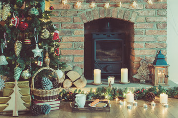Beautiful Christmas setting, decorated fireplace with woodburner, lit up Christmas tree with baubles and ornaments, lantern, stars and garlands, selective focus