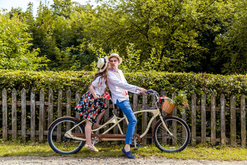 Young couple riding a bike tandem in the park. Against the background of the fence from the tree