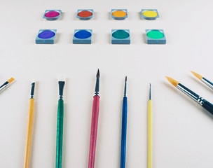 Watercolor and brushes at beige background.