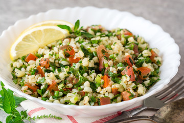 Tabbouleh salad with bulgur, tomatoes, parsley, green onion and mint in plate on grey stone table.