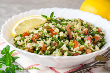 Tabbouleh salad with bulgur, tomatoes, parsley, green onion and mint in plate on grey stone table.