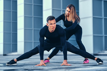 Fototapeta na wymiar Fitness couple is stretching over modern building background.