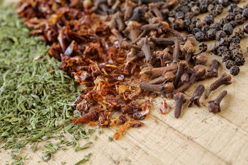 Extreme close up of herbs and spices on a wooden cutting board. Macro shot of savory, paprika, clove and pepppercorn