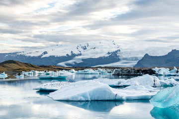 Glacial lagoon in Iceland, cloudy weather, mountains on the horizon. The glacial lake reflects the sky