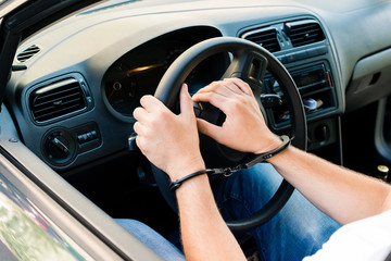 handcuffed hands of an offender sitting behind the wheel of a car. Concept of arrest the driver,...