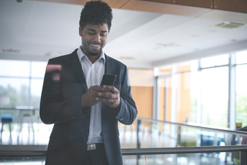 Fototapeta premium African business man standing in business building. Business man reading on smart phone.