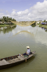 Asian fisherman with boat on river, fisher net in backgound, Hoi An, Vietnam