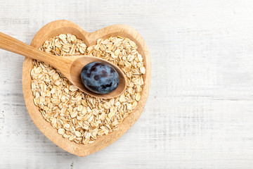 Dry oat flakes and plum in heart shaped wooden bowl