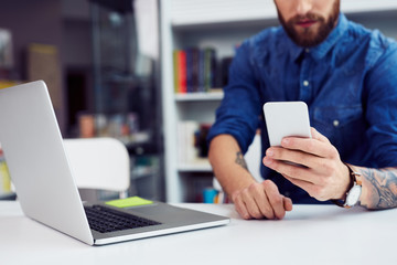 Close-up of a young male student using phone and laptop in campus library