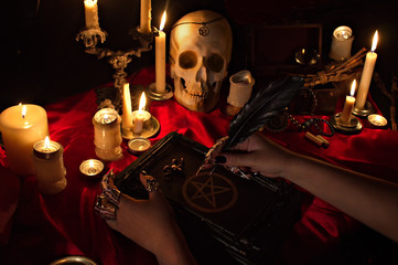 Witchcraft composition with witch's hands holding a quill, satanic magic book with pentagram...