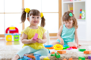 Children playing together. Toddler kids play with blocks. Educational toys for preschool and kindergarten child. Little girls build pyramid toys at home or daycare.