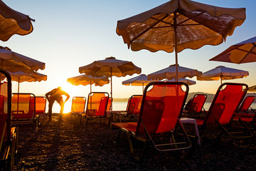 Silhouette view of public beach sun with umbrellas with loungers next to the coastline