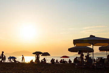 Fototapeta na wymiar Silhouette view of people, tourists next to the coastline sun umbrellas